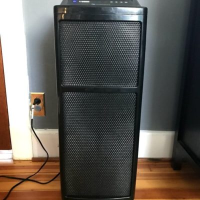 A black Intellipure Air Purifier is set up inside of a home with hardwood floors and a gray wall.