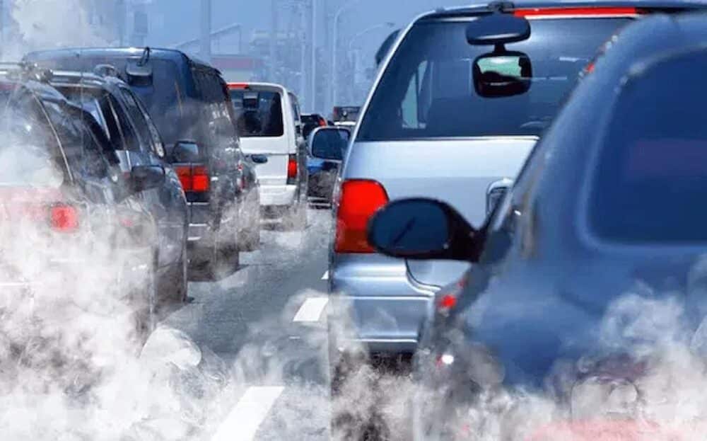 The back of cars in traffic on the road are pictured with exhaust smoke filling the air