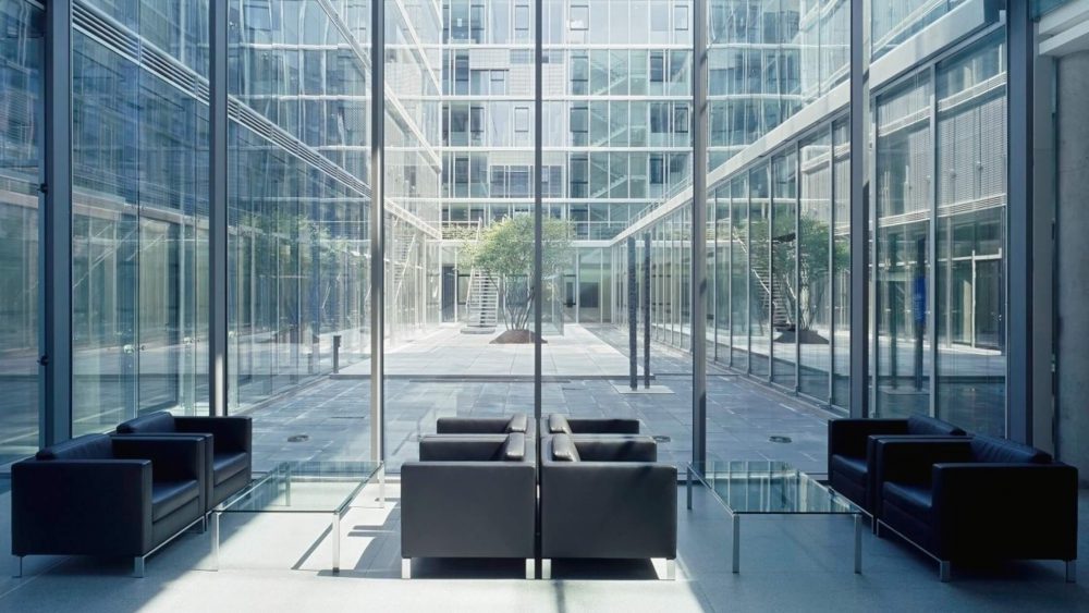 The inside of a building's waiting area that has floor-to-ceiling windows and black and gray leather arm chairs.