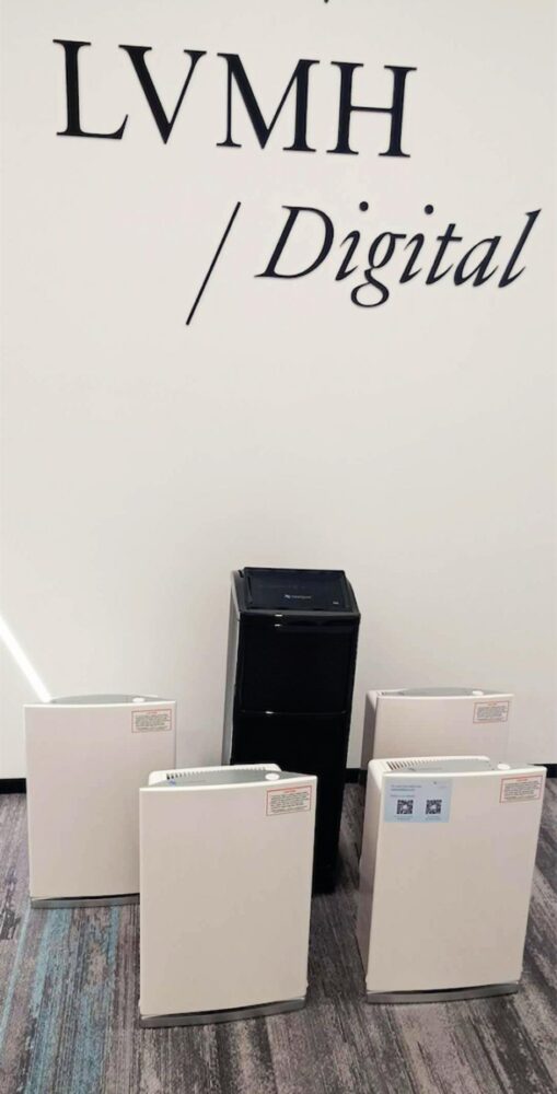 Five Intellipure Air Purifiers are displayed against a wall that says "LVMH / Digital" in black writing inside of a building.